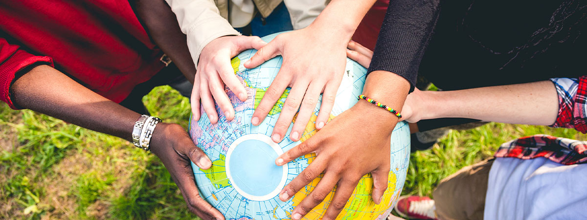 closeup of hands of diverse skin colors holding a large globe