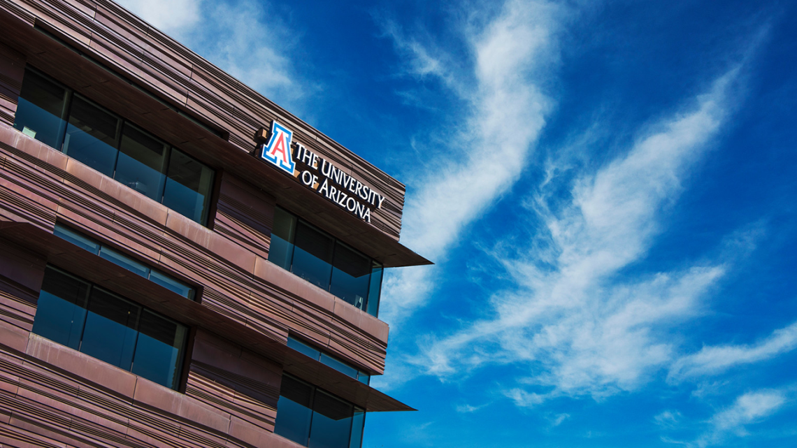 University of Arizona logo on a building surrounded by blue sky.