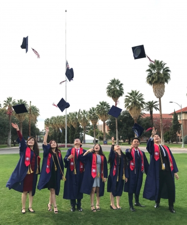 University of Arizona International Student graduates wearing camps and gowns, throwing caps in the air in celebration
