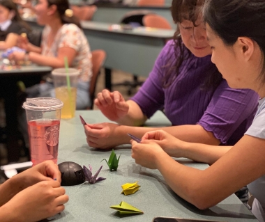 three people folding origami paper cranes at a table