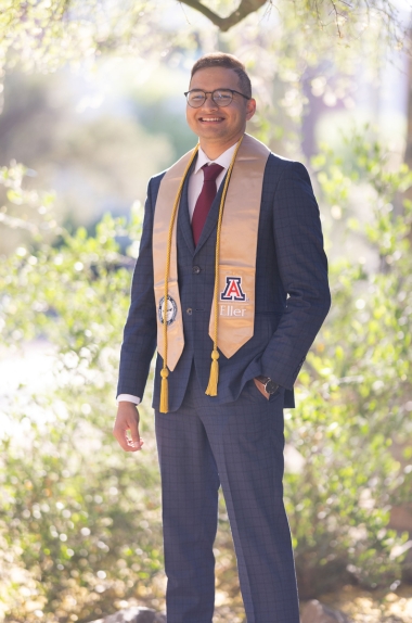 Jiten standing in a garden, in a navy blue suit and wearing Eller College of Management graduation stole