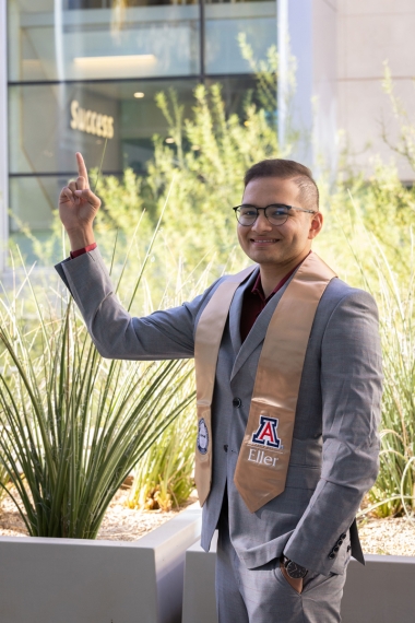 Jiten is wearing a grey suit and Eller stole and pointing to a sign that says success